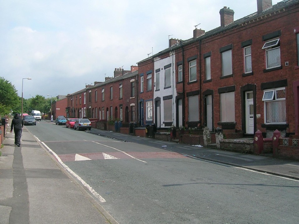 A red brick terraced street with cars parked outside the front doors, Oldham